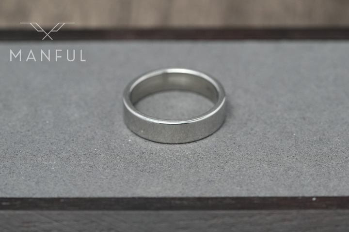 Simple 6mm Ring Silver, standing upright on a pale card surface beside dark wood