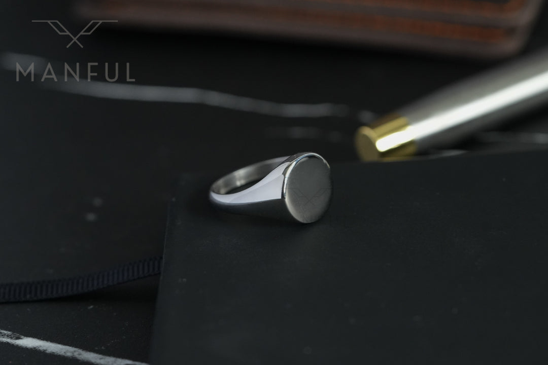 Classic Silver Signet Ring, resting on a black notebook beside a pen on a desk