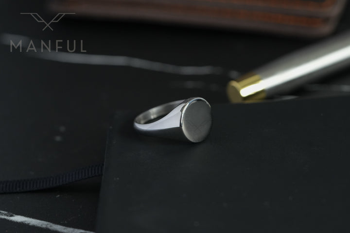 Classic Silver Signet Ring, resting on a black notebook beside a pen on a desk