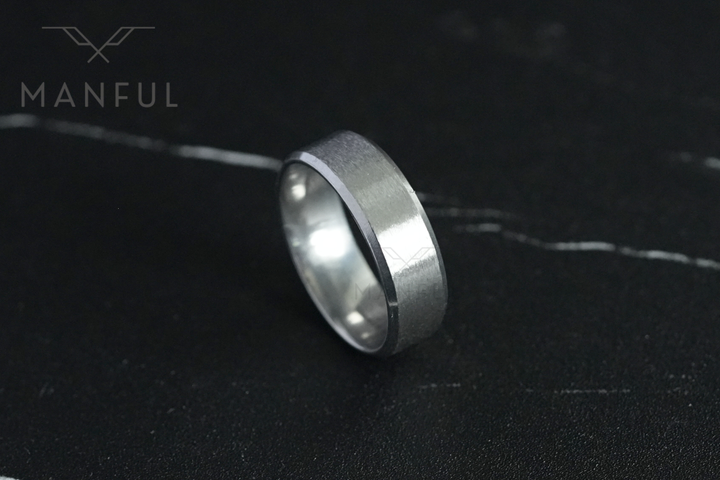 Simple Stainless Steel Ring 8mm Silver, angled on a dark veined marble surface with the Manful logo