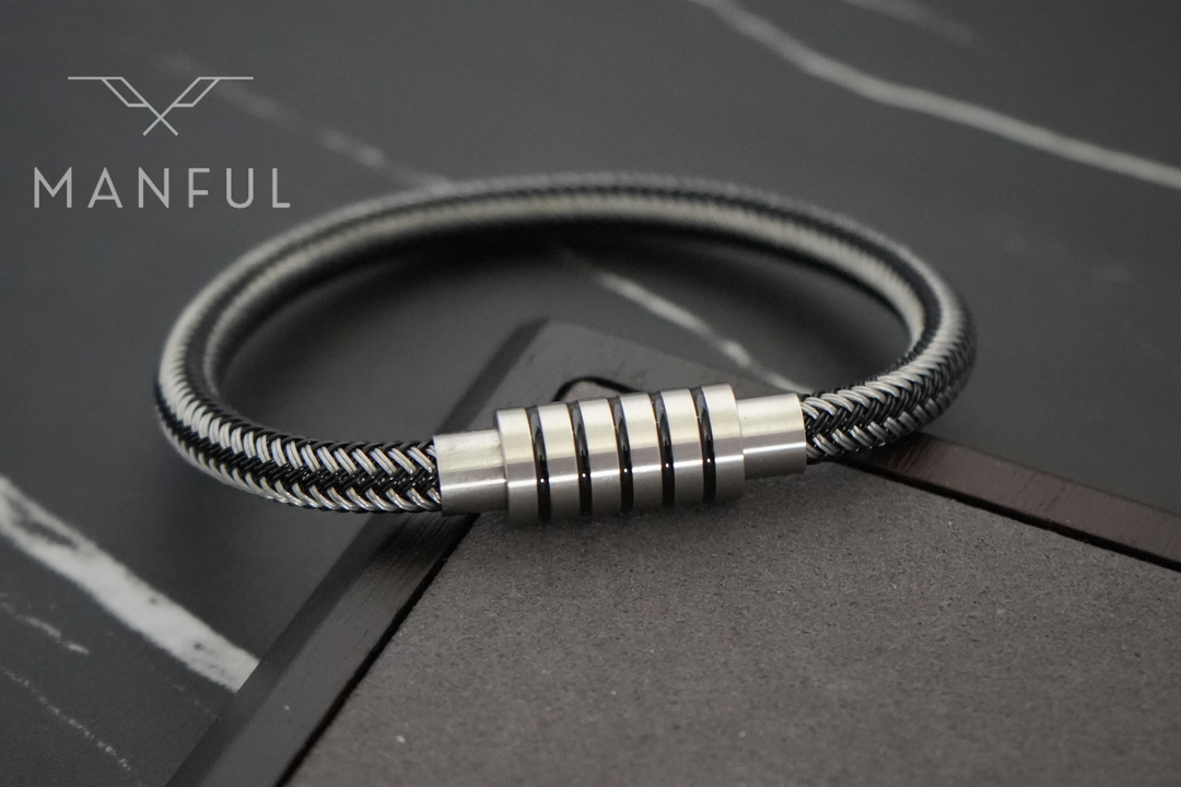 Steel Wire Bracelet Black, propped on a dark marble surface beside a wooden corner