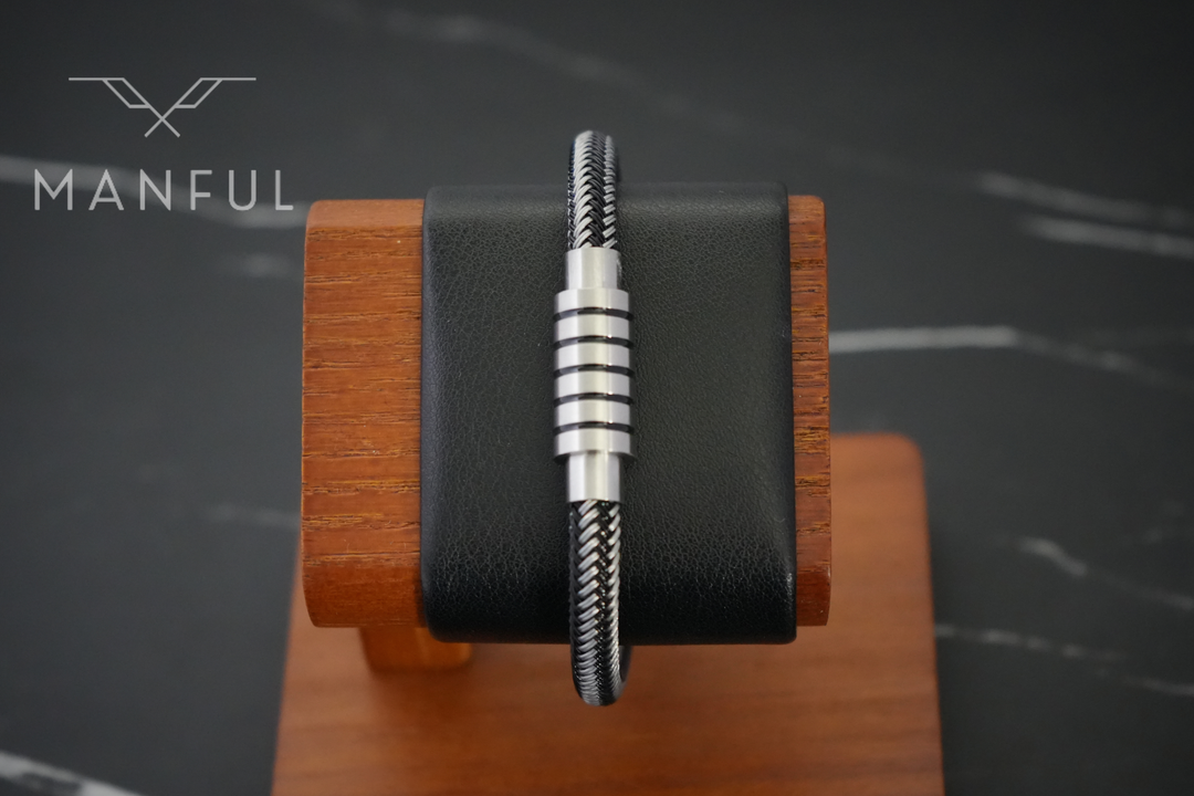 Steel Wire Bracelet Black, displayed upright on a wooden stand with a black leather cushion