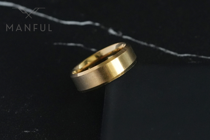 Simple Stainless Steel Ring 8mm Gold, leaning against a dark box edge on marble