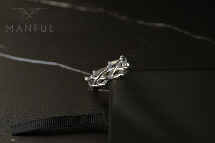 Thorn Ring Silver, resting on a dark marble surface beside a black ribbon