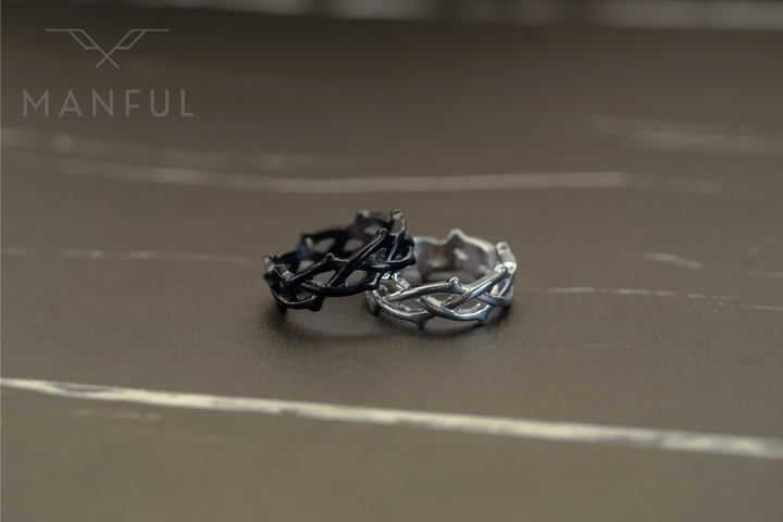 Thorn Ring Silver, standing beside a matching black thorn ring on a brown surface