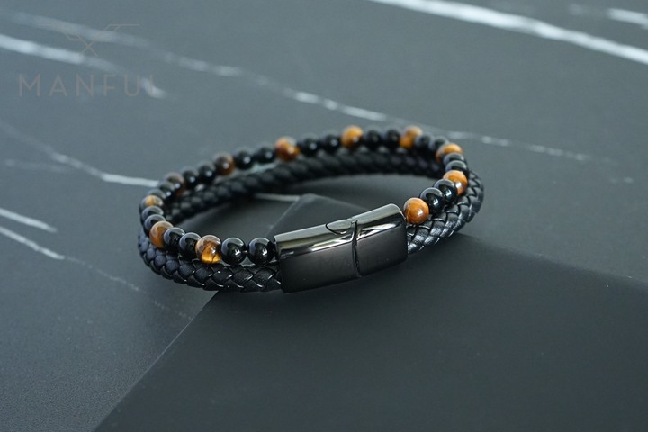 Tigers Eye Bead And Leather Bracelet, curved over a dark stone slab edge, clasp catching light