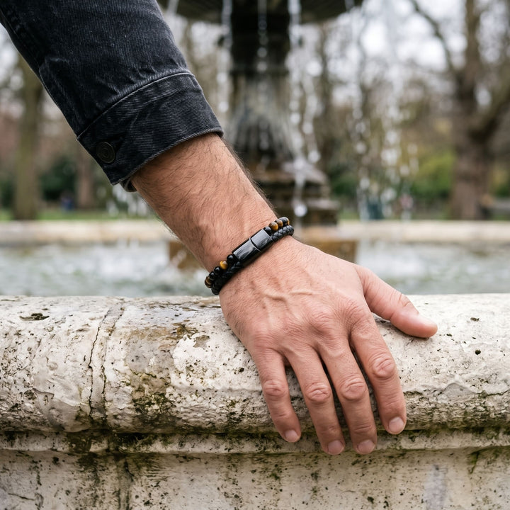 Tigers Eye Bead And Leather Bracelet on a man's wrist, his hand resting on the stone rim of a fountain