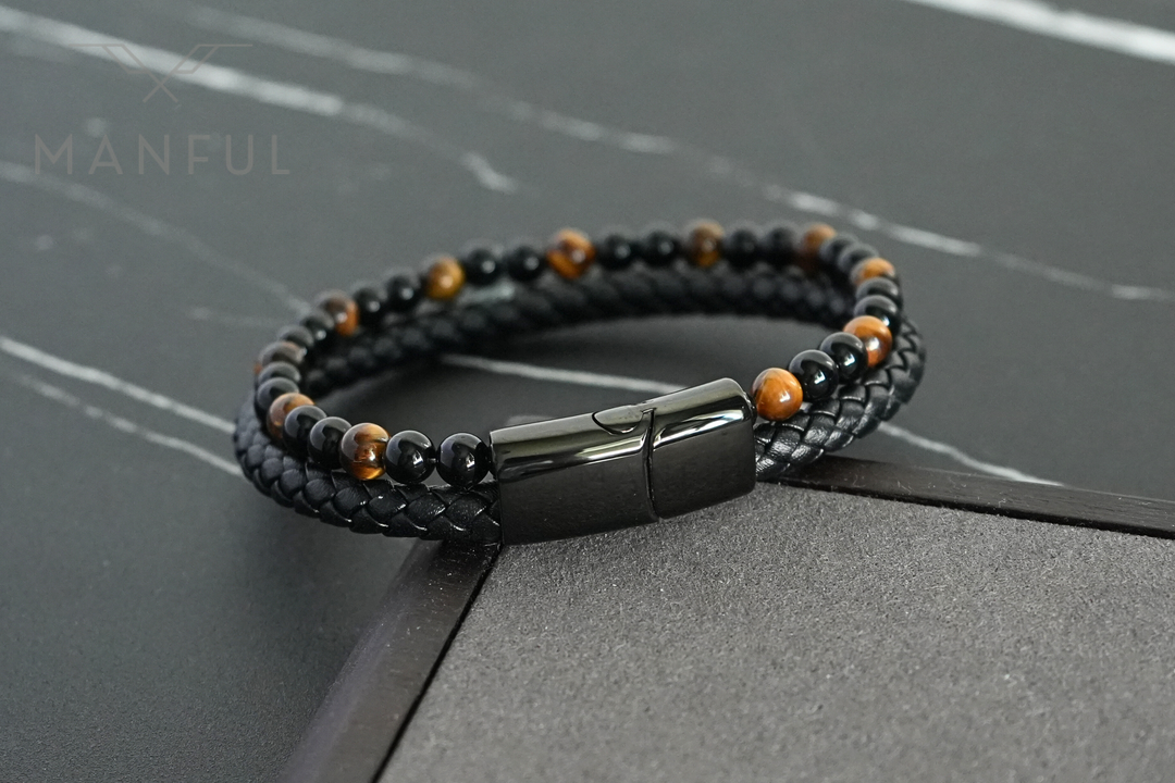 Tigers Eye Bead And Leather Bracelet, angled on a dark surface beside a stone corner prop