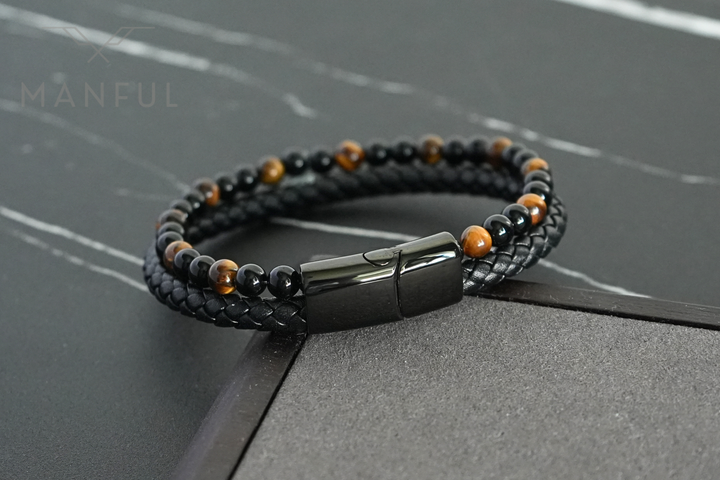 Tigers Eye Bead And Leather Bracelet, angled on a dark surface beside a stone corner prop