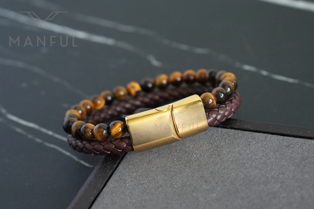 Tigers Eye Bead And Leather Bracelet Gold, propped on a raised dark stone block at an angle