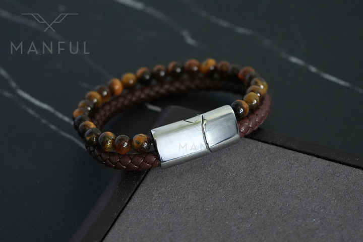 Tigers Eye Bead And Leather Bracelet Silver, resting on dark slate beside a raised stone ledge