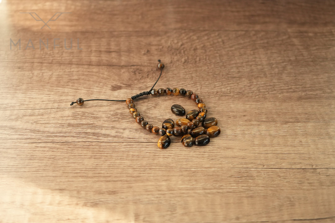 Tigers Eye Bead Bracelet, coiled loosely on a wood table with its cord trailing