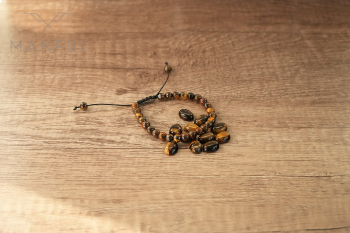 Tigers Eye Bead Bracelet, coiled loosely on a wood table with its cord trailing