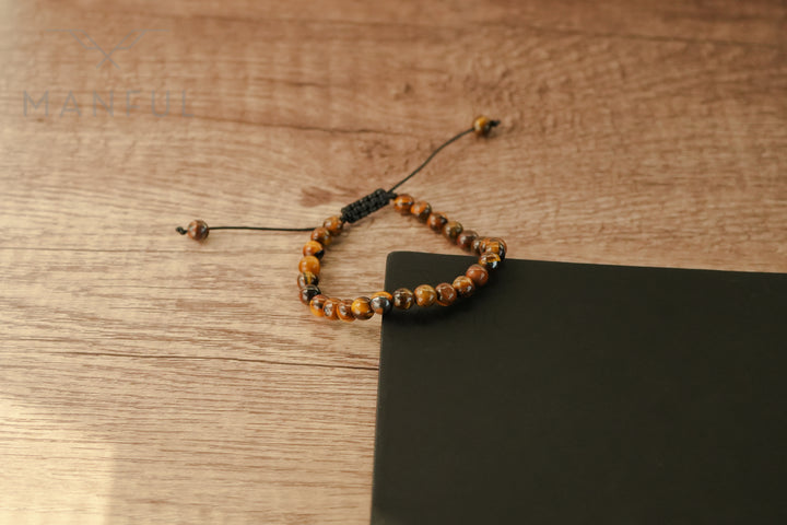 Tigers Eye Bead Bracelet, laid in a loop on wood beside a black card corner