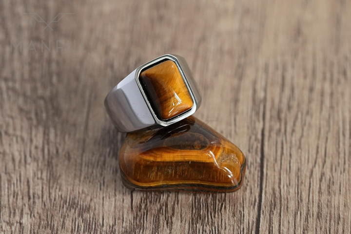 Tigers Eye Signet Ring Silver, leaning against a raw tiger's eye crystal on a wood surface