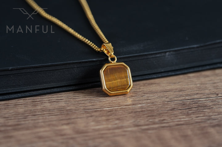 Tigers Eye Square Necklace Gold, resting against a black book on a wood table