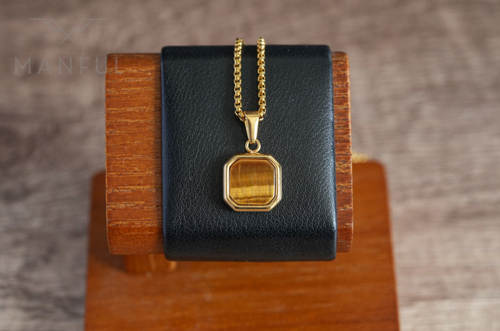 Tigers Eye Square Necklace Gold, displayed hanging on a black leather stand on a wood block