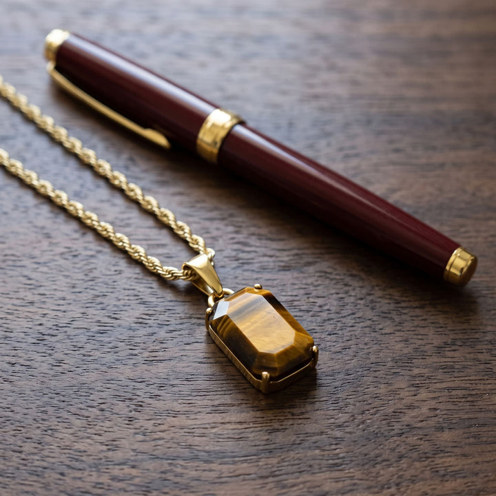 Tigers Eye Stone Pendant (Gold) on a walnut desk beside a burgundy fountain pen