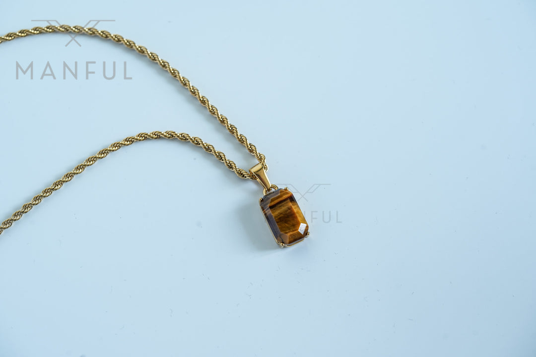 Tigers Eye Stone Pendant Gold, lying flat on a pale blue background with the chain looped beside it