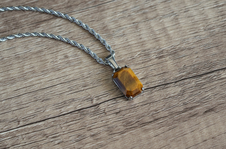 Tigers Eye Stone Pendant Silver, flat lay on a wood surface with the chain coiled above it