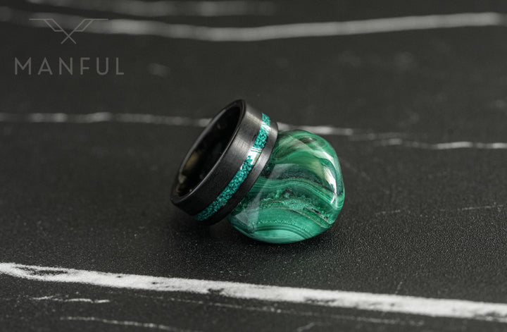 Tungsten Malachite Inlay Band Black, resting on its side against a polished malachite stone