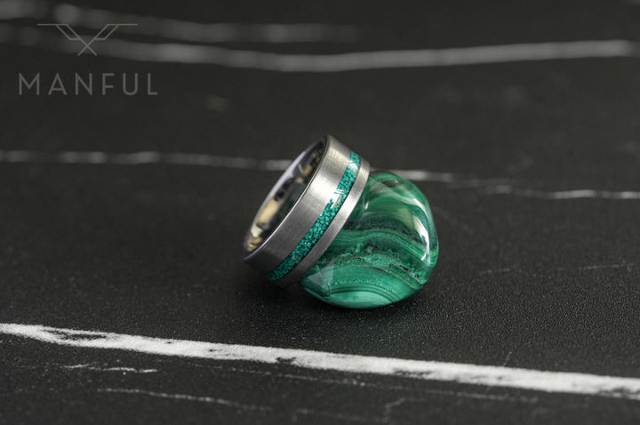 Tungsten Malachite Inlay Band Silver, resting against a raw malachite stone on a dark marble surface
