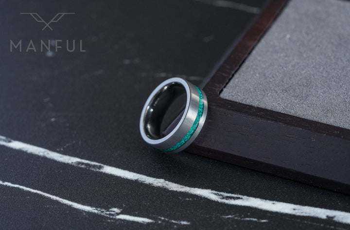 Tungsten Malachite Inlay Band Silver, balanced on the edge of a dark wooden block