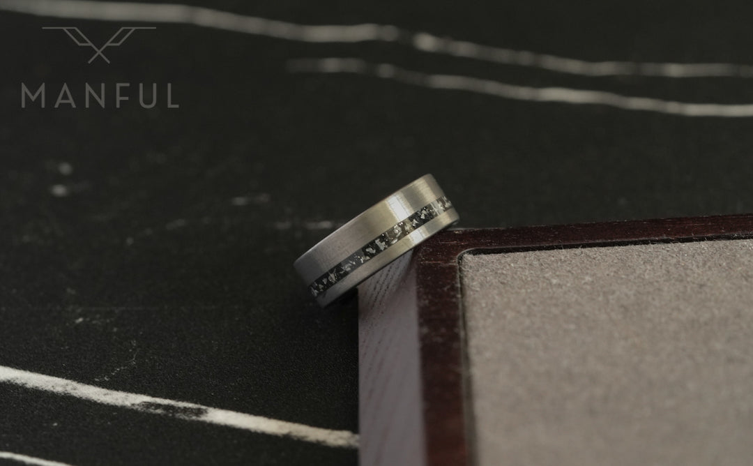 Tungsten Meteorite Inlay Band Silver, balanced on the corner of a wooden box on a dark surface