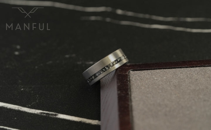 Tungsten Meteorite Inlay Band Silver, balanced on the corner of a wooden box on a dark surface