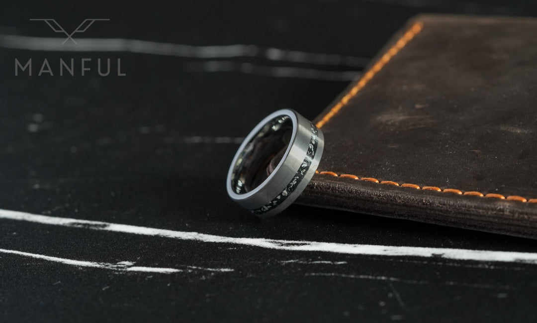 Tungsten Meteorite Inlay Band Silver, leaning against a leather book with orange stitching