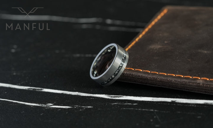 Tungsten Meteorite Inlay Band Silver, leaning against a leather book with orange stitching