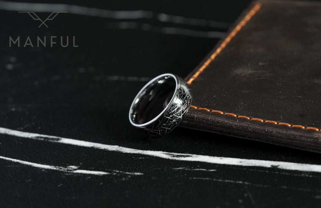 Meteorite Fragment Ring, leaning against a leather book with orange stitching on dark slate