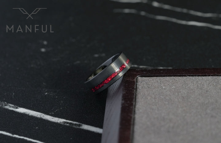 Tungsten Red Opal Inlay Band Black, tilted against a dark book corner on a marble surface