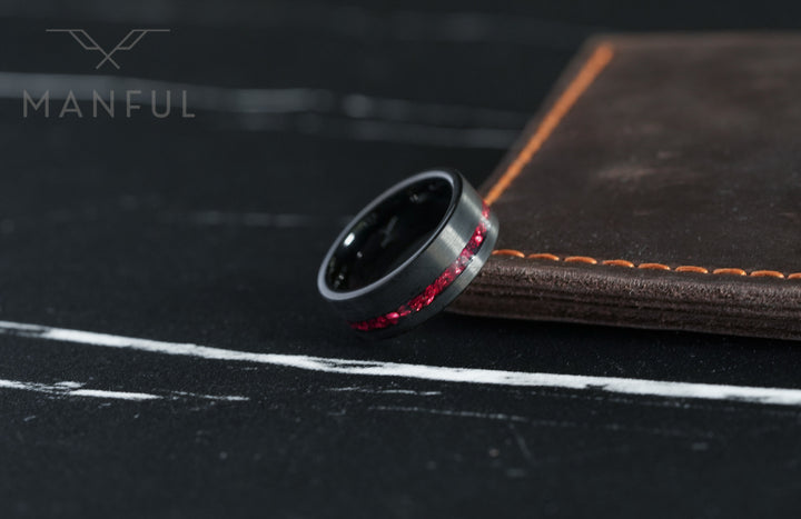 Tungsten Red Opal Inlay Band Black, leaning against a brown leather book edge showing the inner black lining