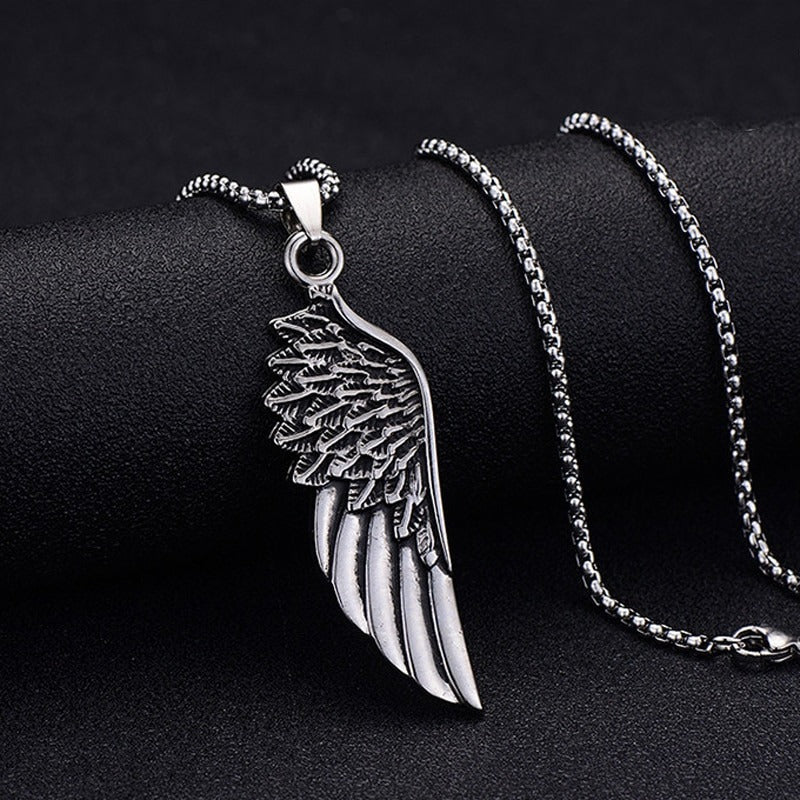 Wing Pendant Necklace, draped over a rounded black stone, chain coiled behind