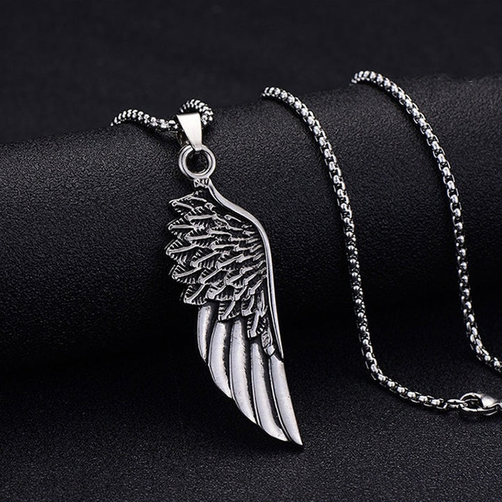 Wing Pendant Necklace, draped over a rounded black stone, chain coiled behind