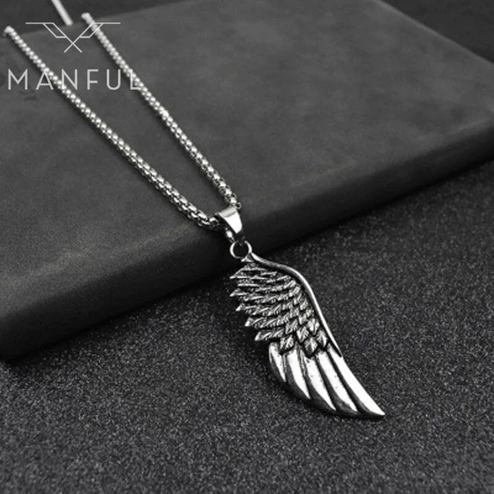 Wing Pendant Necklace, laid flat across the edge of a grey stone block